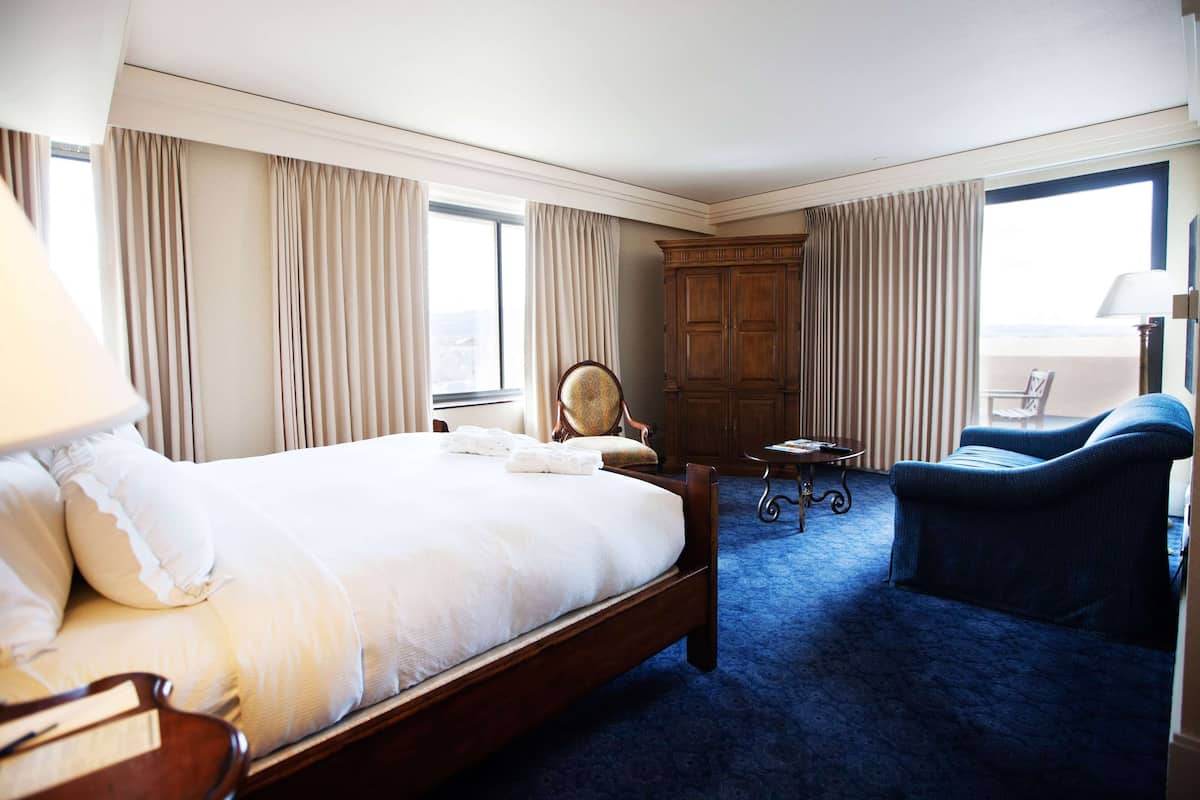 A hotel room with a large bed, a chair, a small table, and a wardrobe.