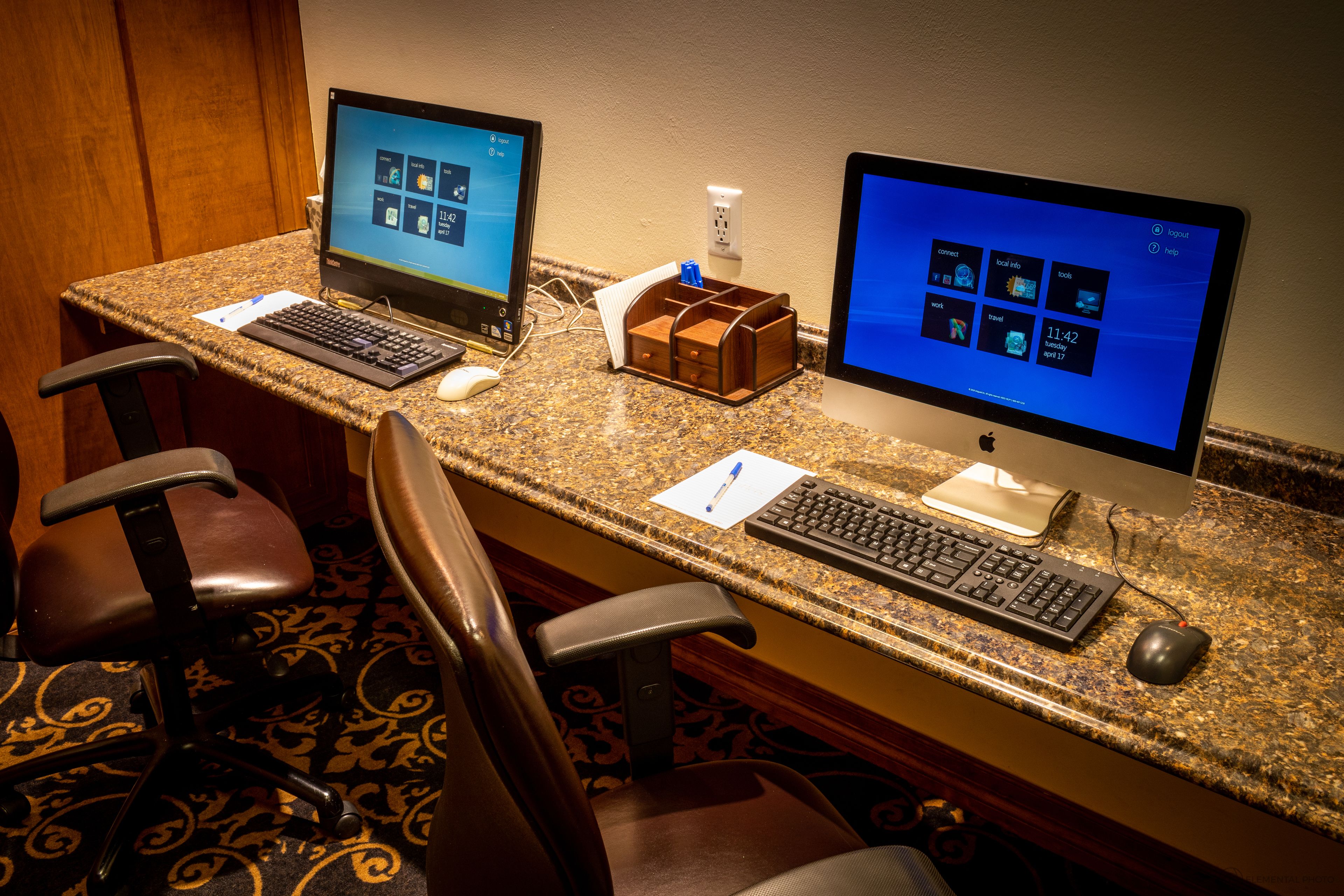 A hotel workspace with two desktop computers, a keyboard, a mouse, and a chair.