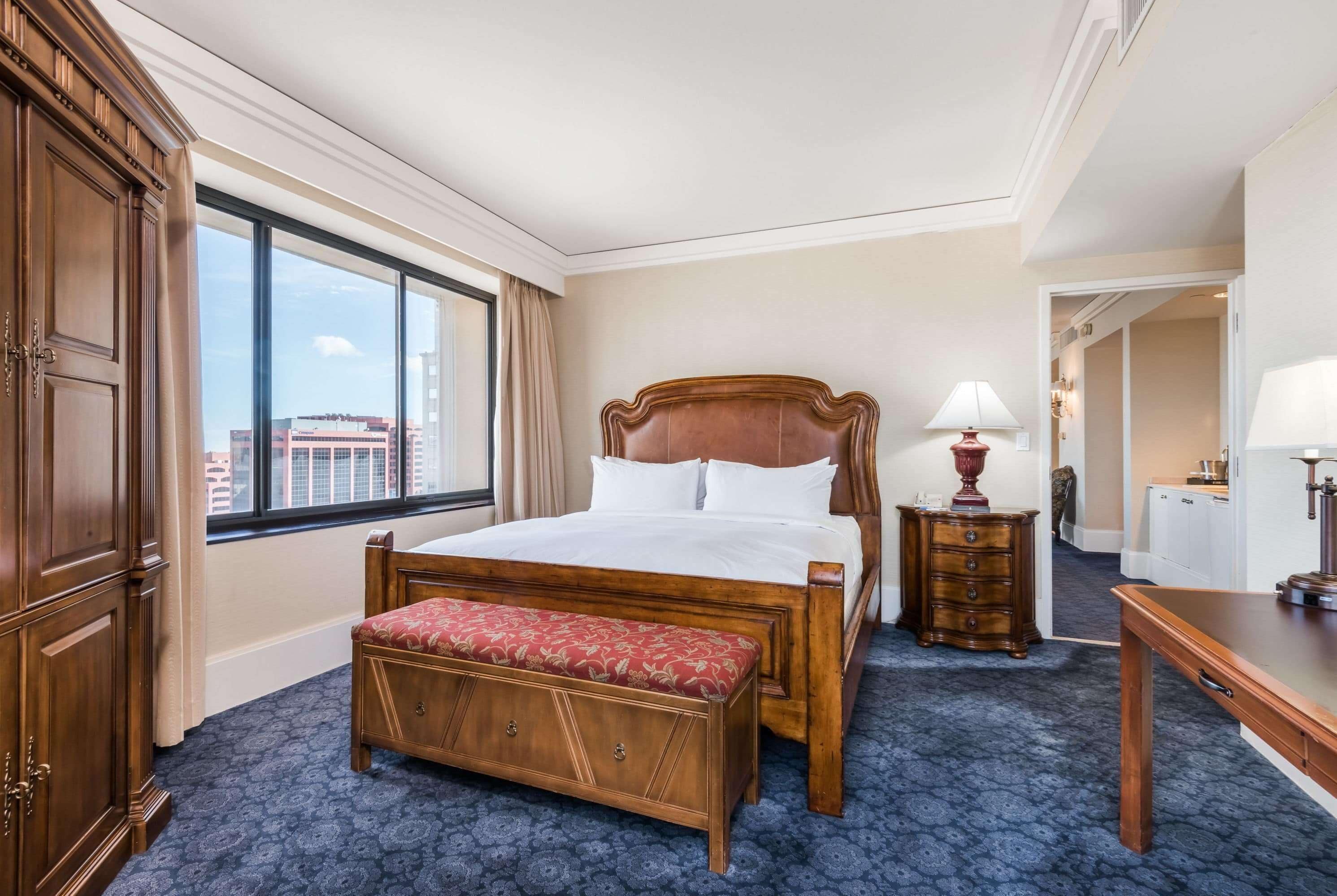A hotel room with a large bed, a wooden bench, a desk, and a dresser.