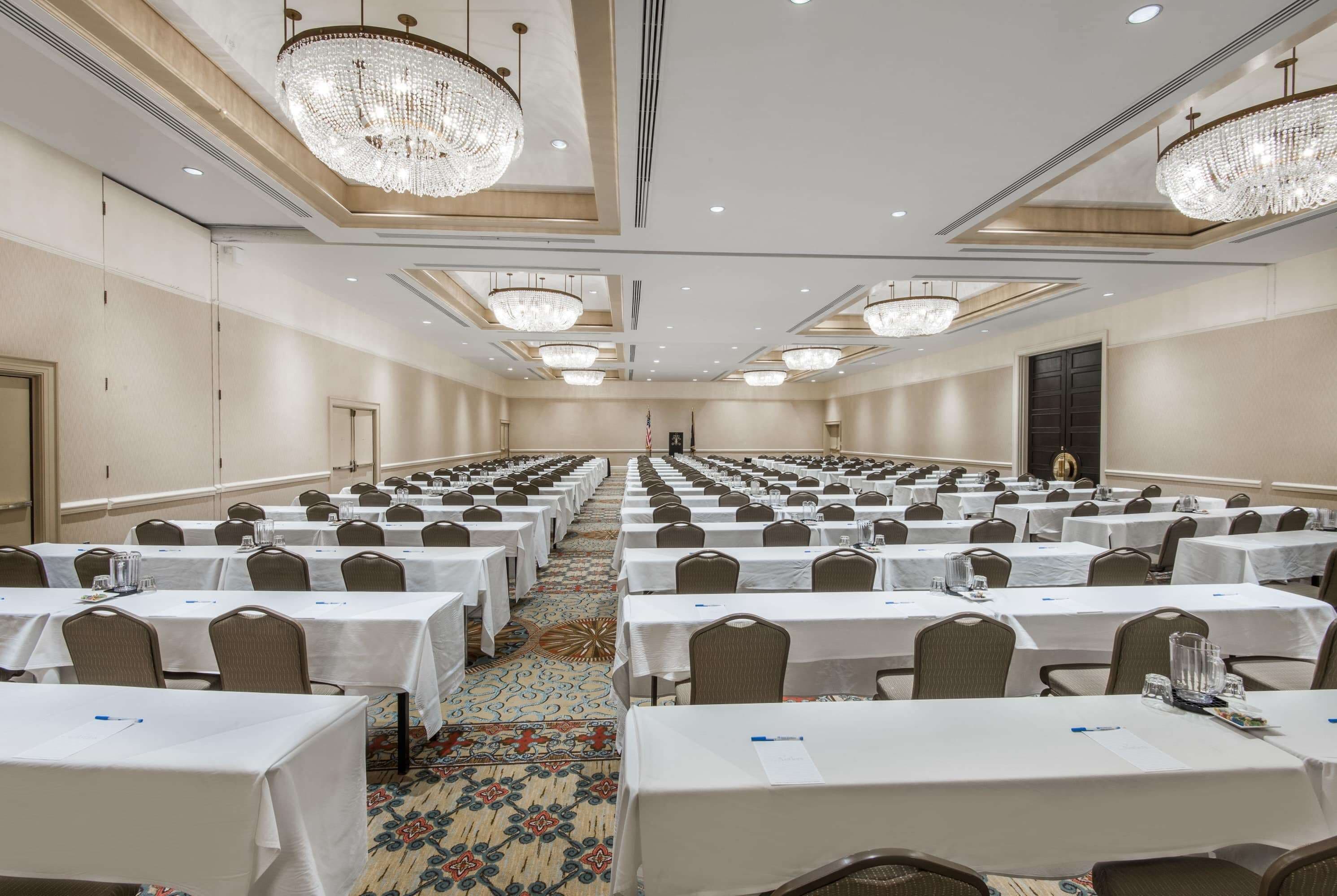 A conference room with rows of tables, chairs, and chandeliers.