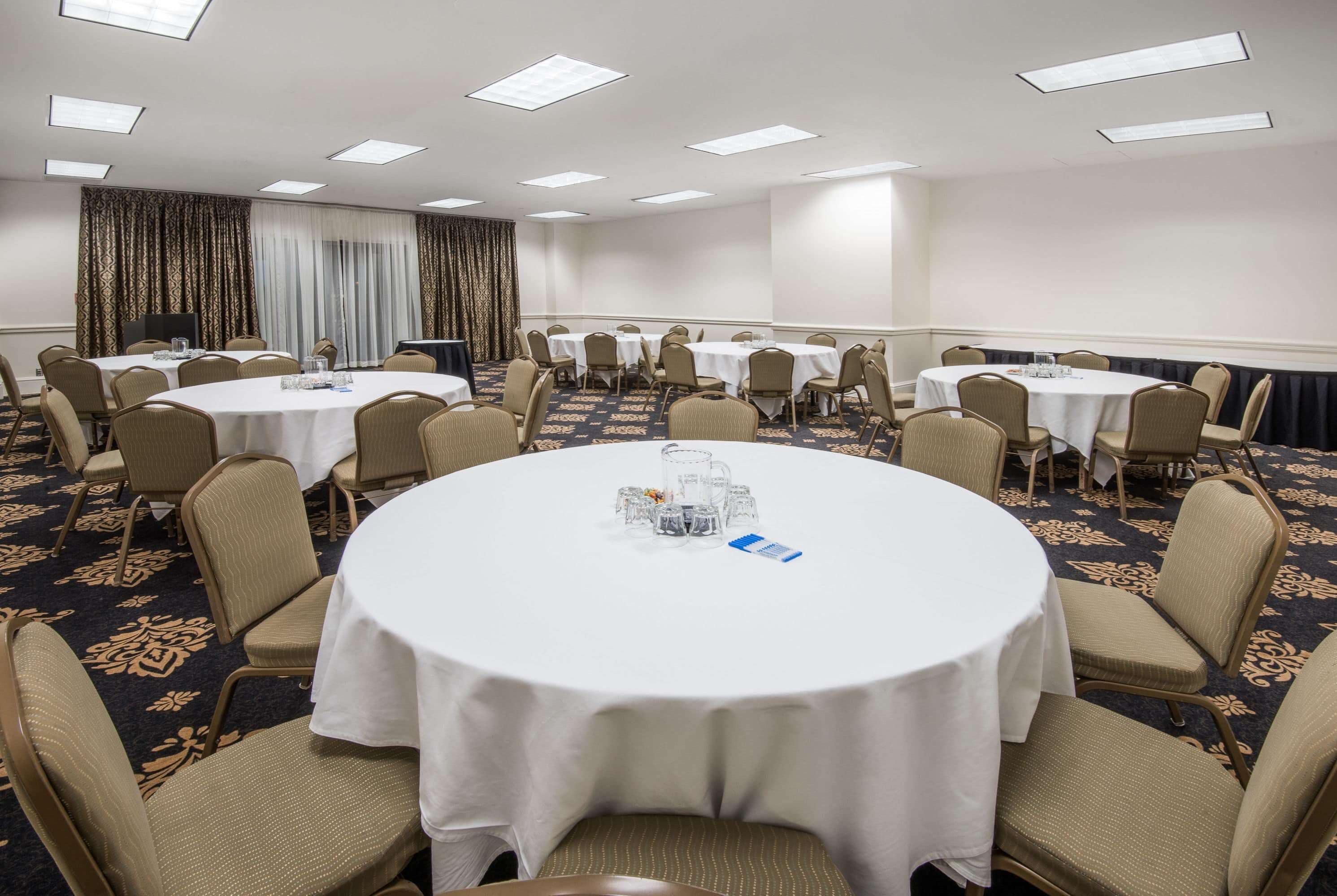 A conference room with round tables, beige chairs, and a carpeted floor.