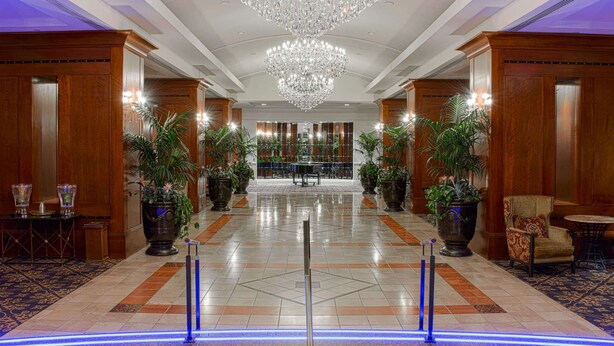 A spacious lobby with a large chandelier, potted plants, and a check-in desk.