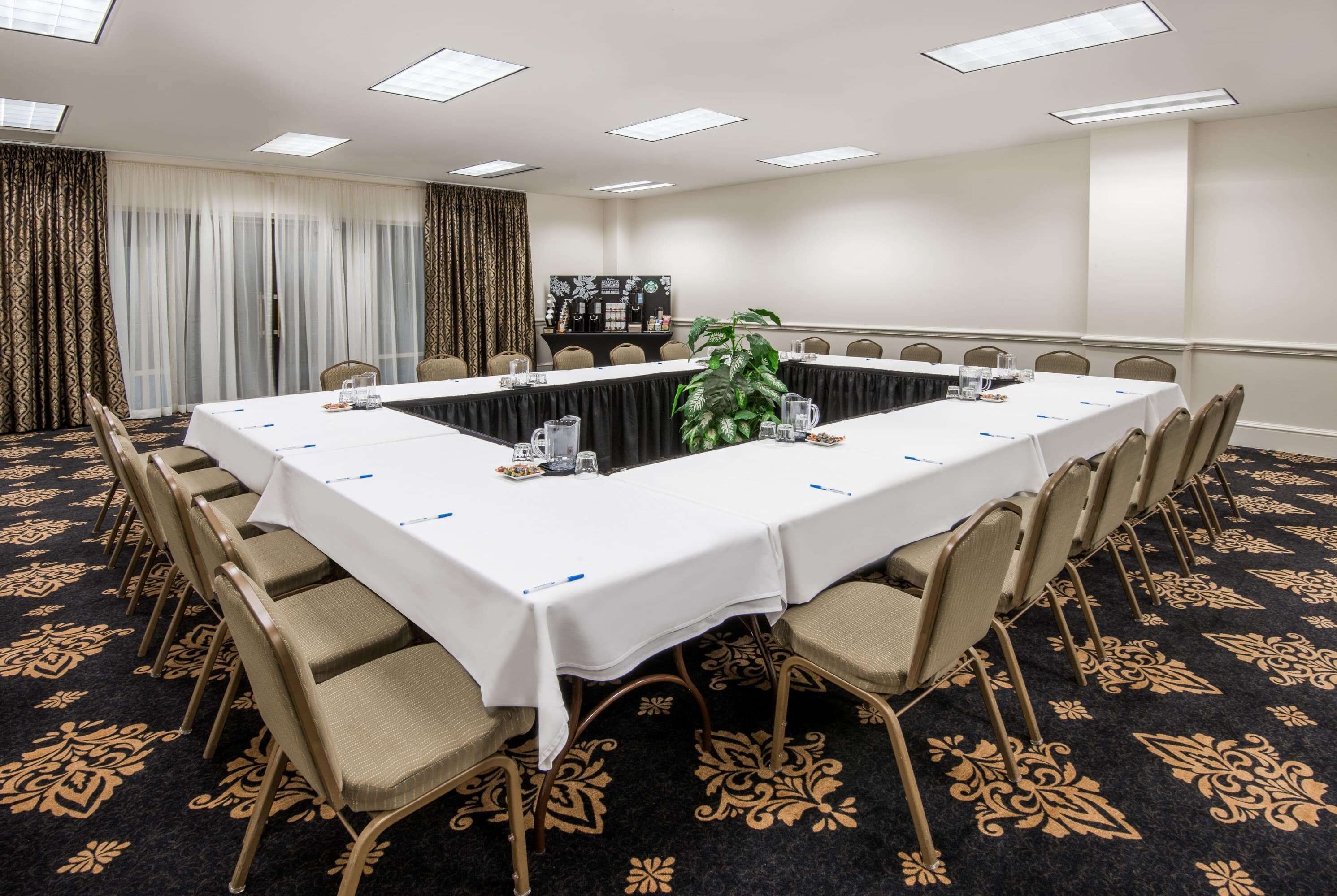 A conference room with a long table, chairs, a coffee station, and a patterned carpet.