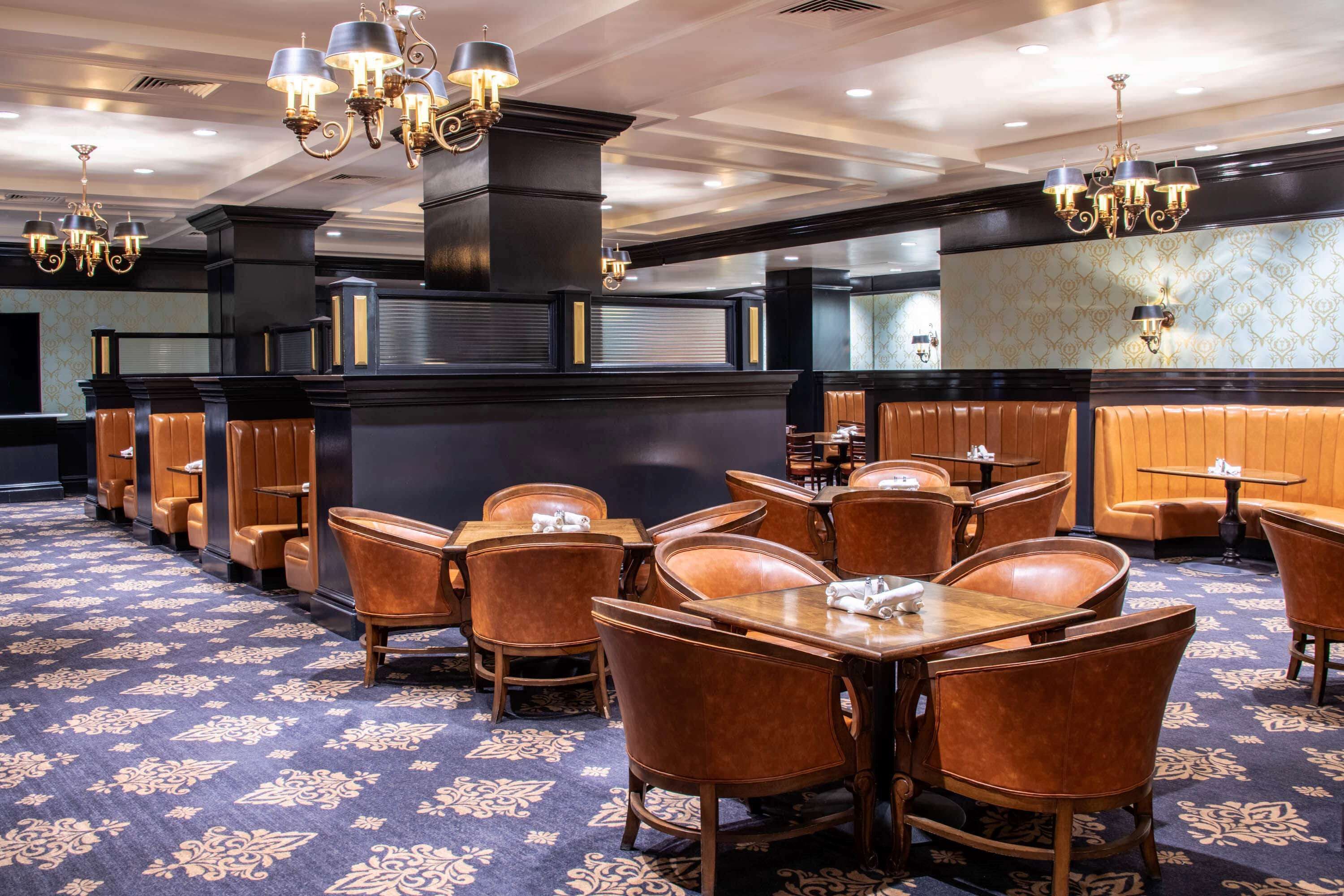 A restaurant with booths and tables, a patterned carpet, and chandeliers.