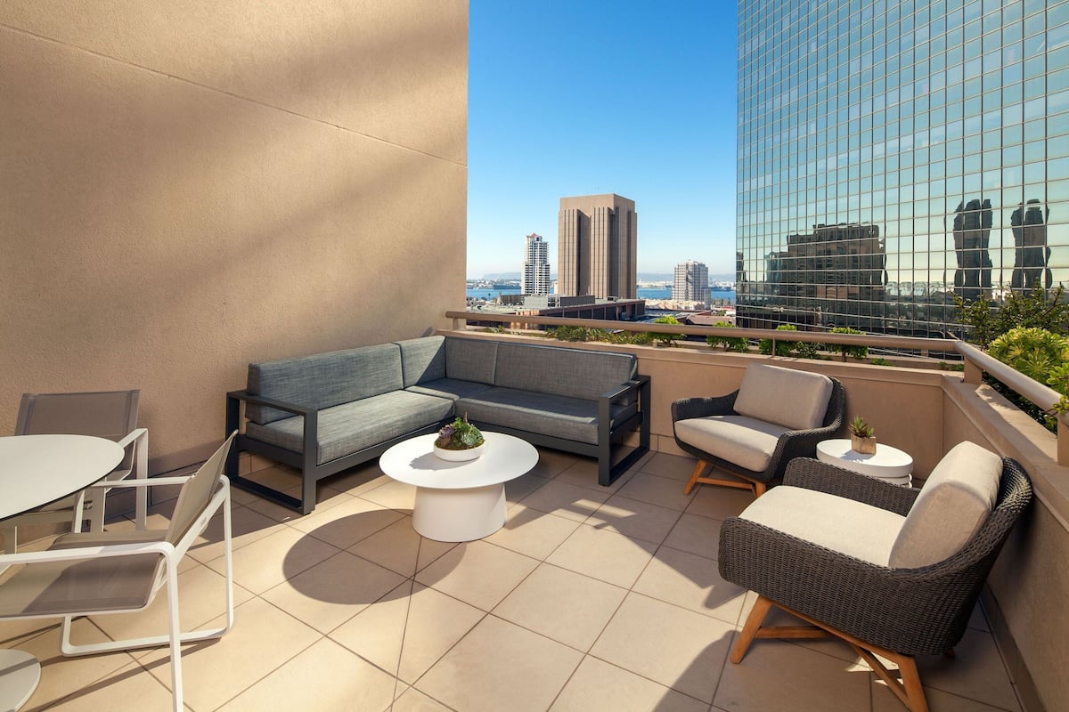 Un espacio exterior moderno con sala, sillones y una mesa de centro, con vistas a un paisaje urbano de edificios altos.
