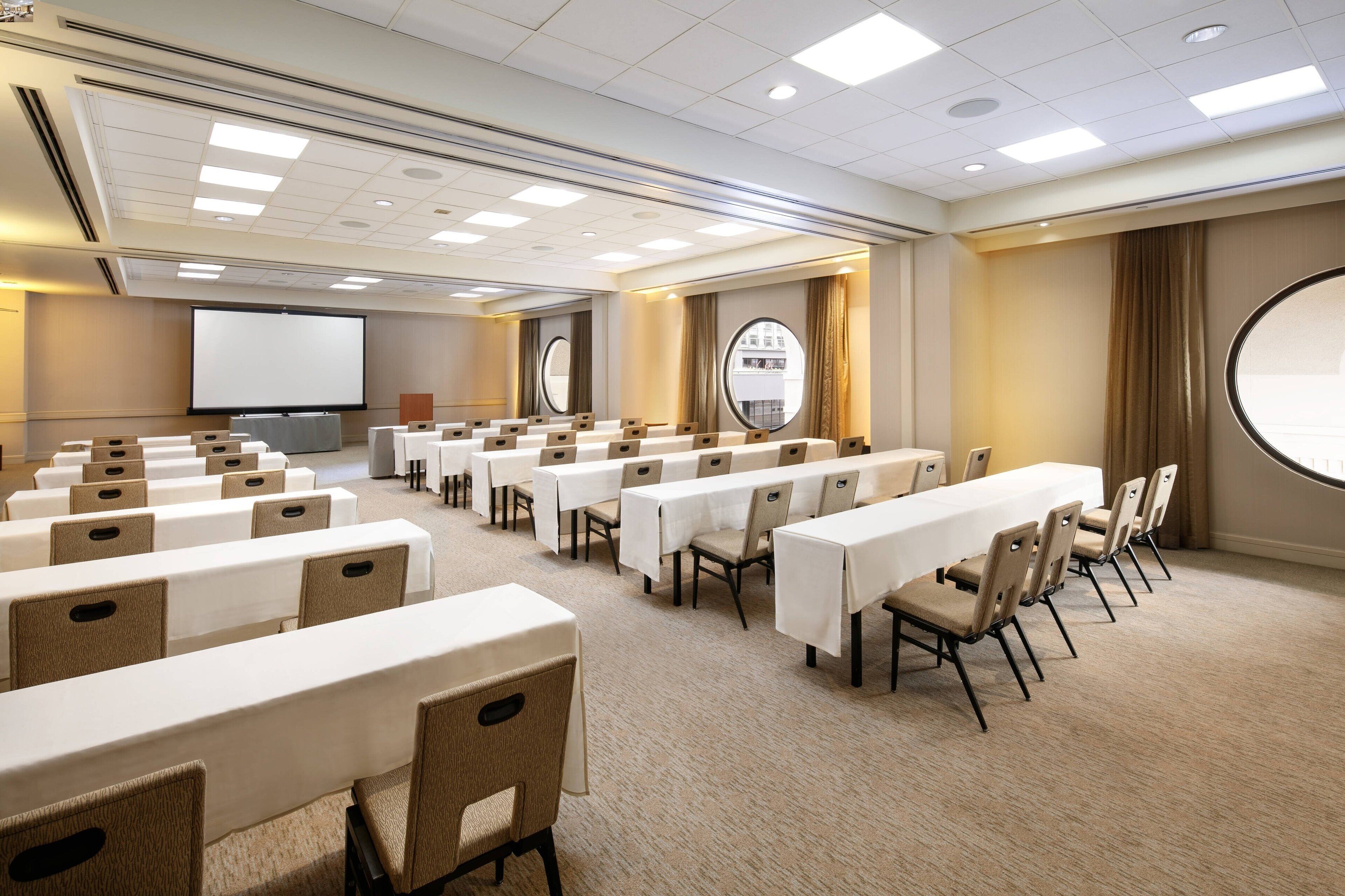 A conference room with multiple tables and chairs, a large screen, and a projector.