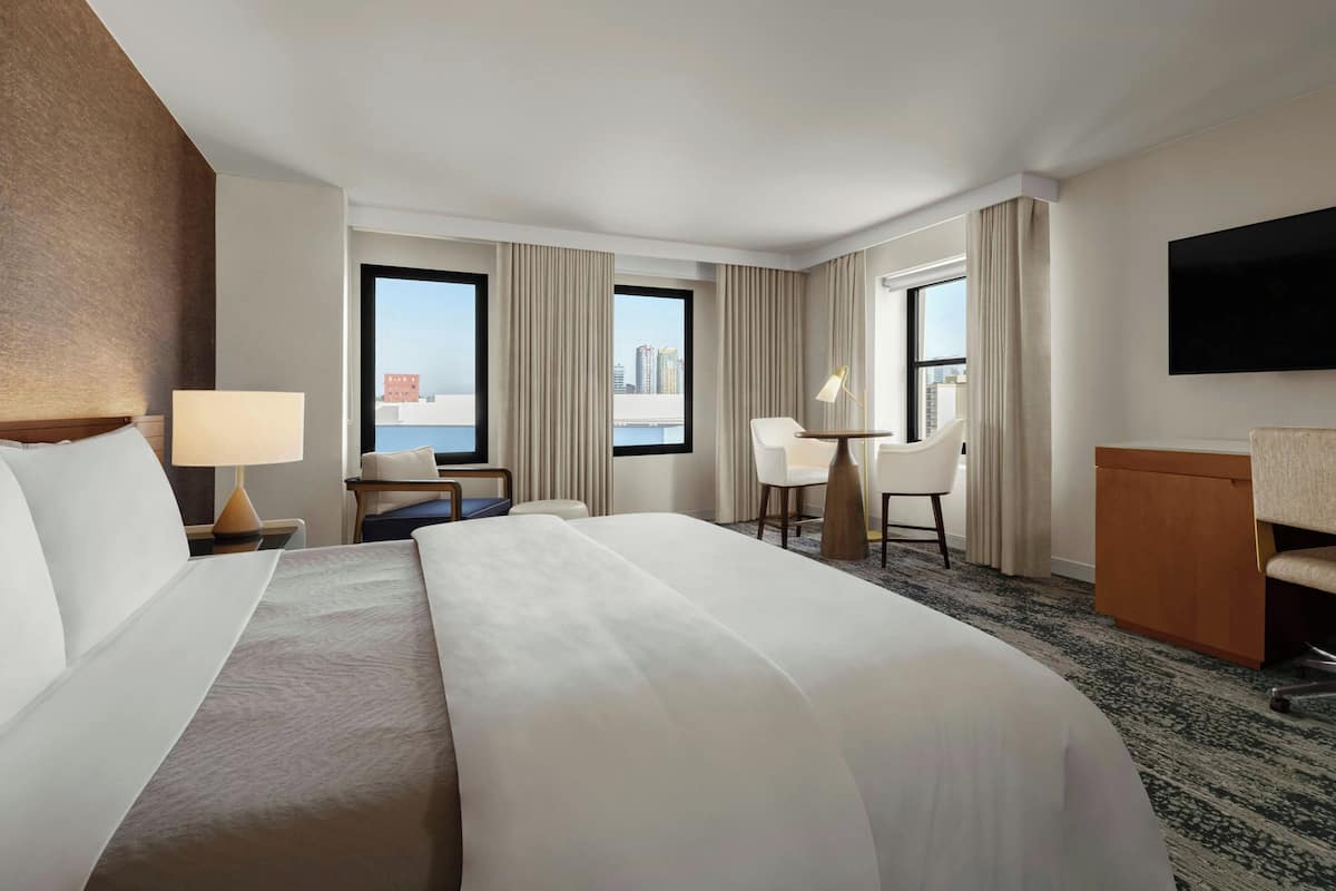Habitación de hotel con una cama grande, un escritorio, dos sillas, un televisor y vistas a la ciudad.