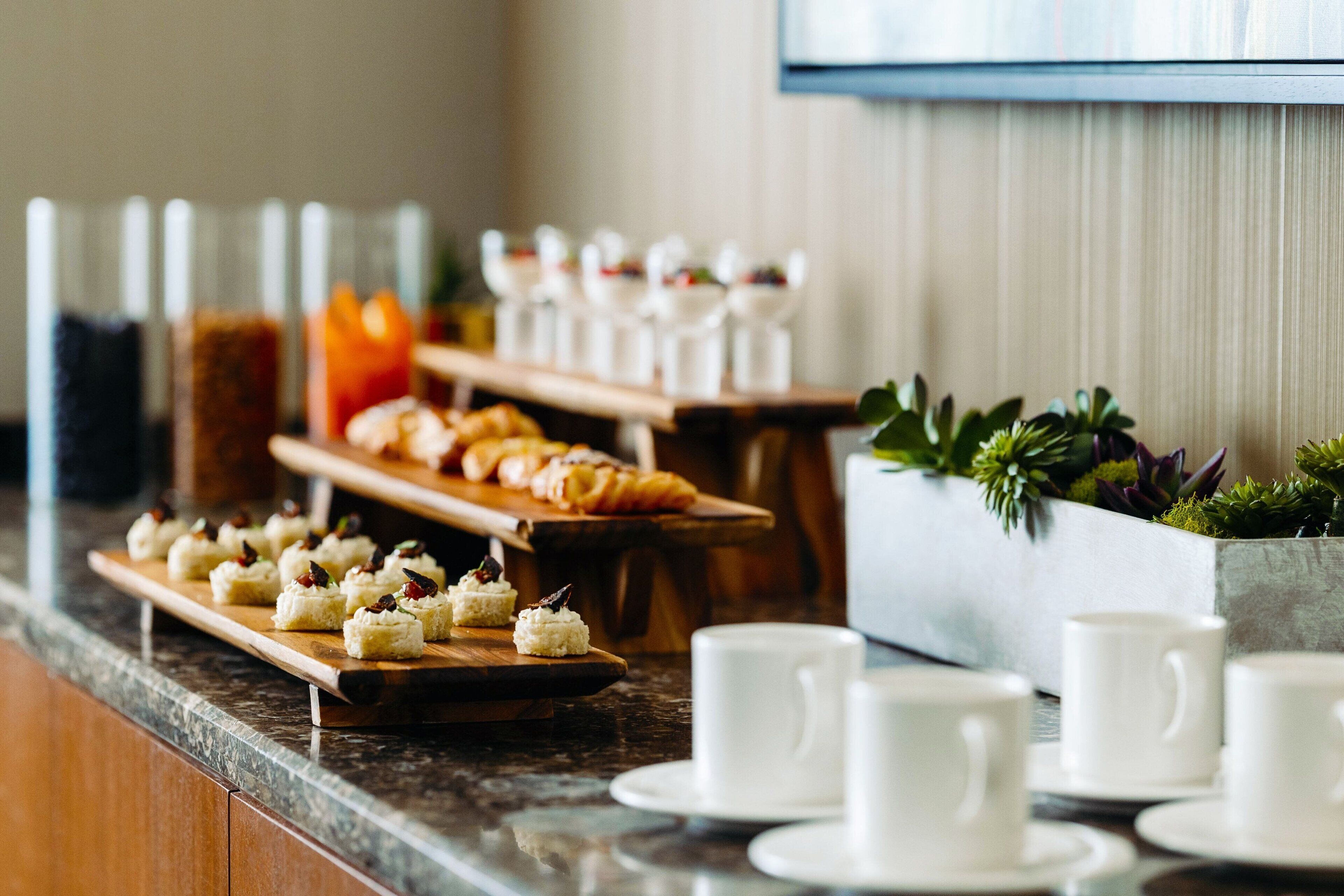 A buffet setup with various food items and white cups on a marble countertop.