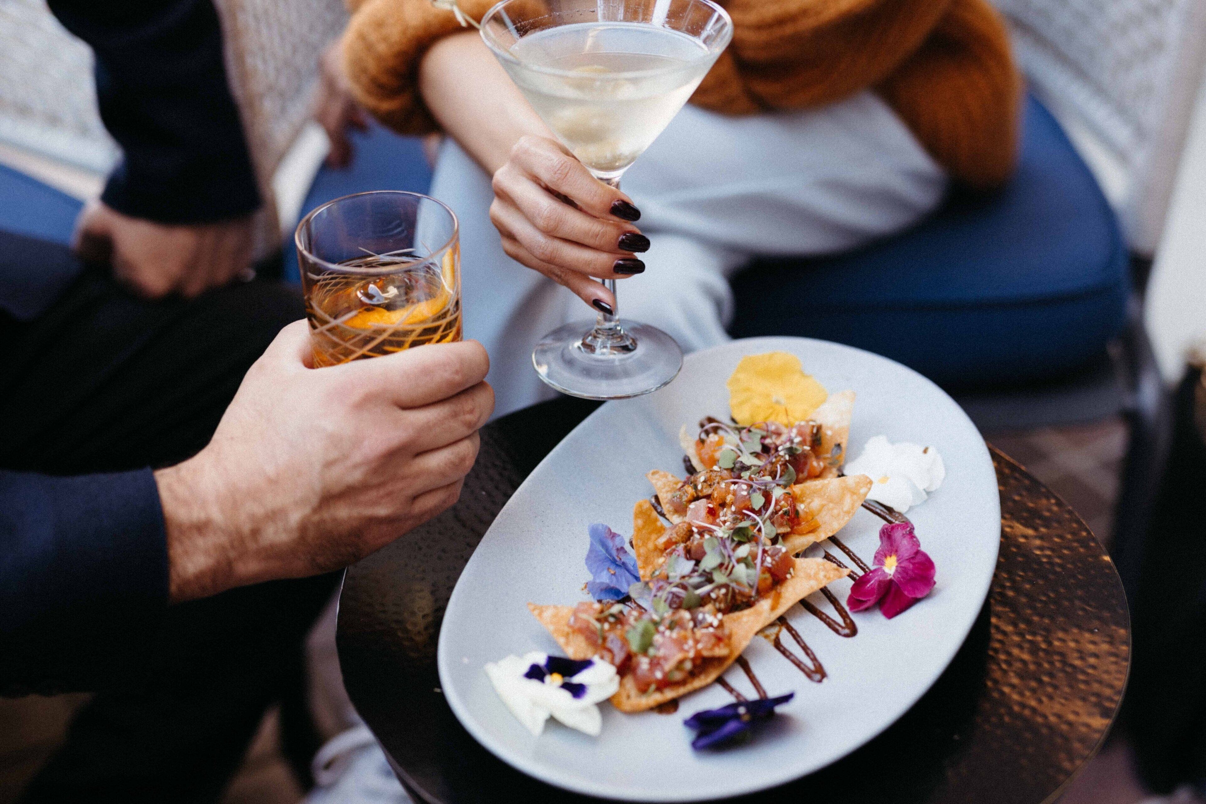A person holding a glass of whiskey and a martini glass with a clear liquid.