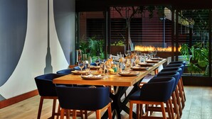 A dining area with a long wooden table set for multiple guests, surrounded by dark blue chairs. - The Westin San Diego Gaslamp Quarter (San Diego)