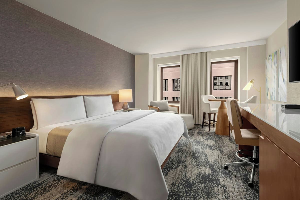 Una habitación de hotel con una cama grande, un escritorio con silla, un televisor y una ventana con cortinas.