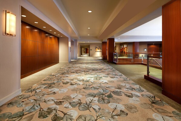 A hotel corridor with a floral carpet, wooden paneling, and recessed lighting.