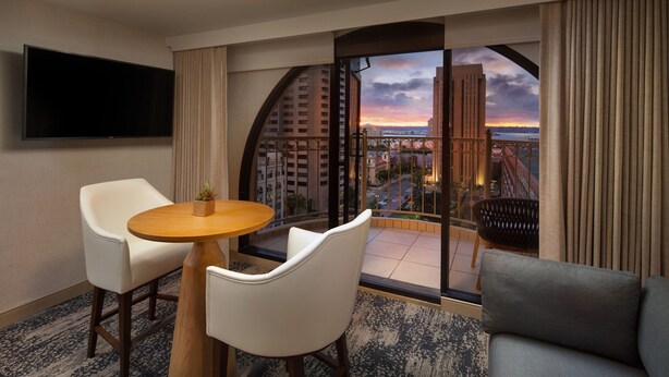 A hotel room with a balcony, a TV mounted on the wall, a round wooden table with two white chairs, and a grey sofa. - The Westin San Diego Gaslamp Quarter (San Diego)