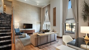 A modern living room with a sofa, coffee table, and TV. There is a staircase leading to another level, and a large window with curtains. - The Westin San Diego Gaslamp Quarter (San Diego)