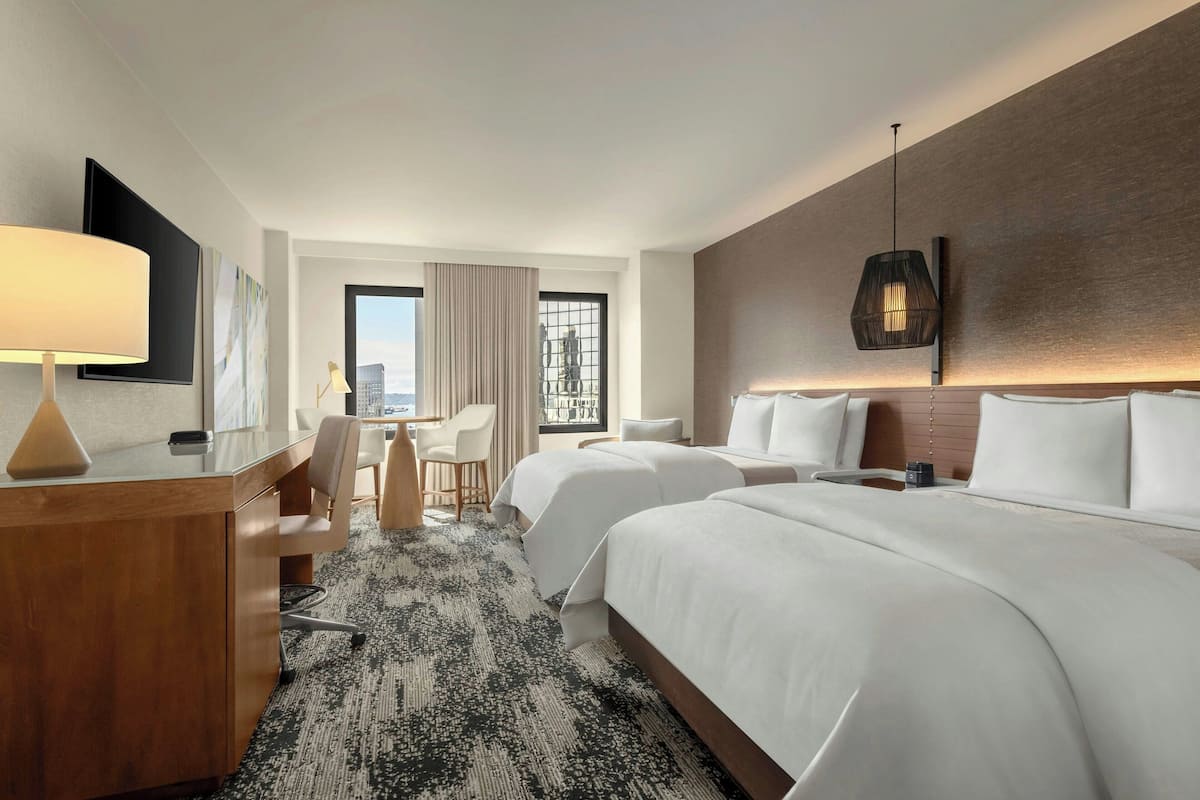 Habitación de hotel con una cama grande, un escritorio, una silla, un televisor y vistas a la ciudad.