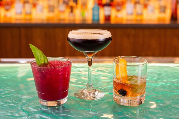 Tres bebidas sobre una barra, con un fondo borroso de botellas.