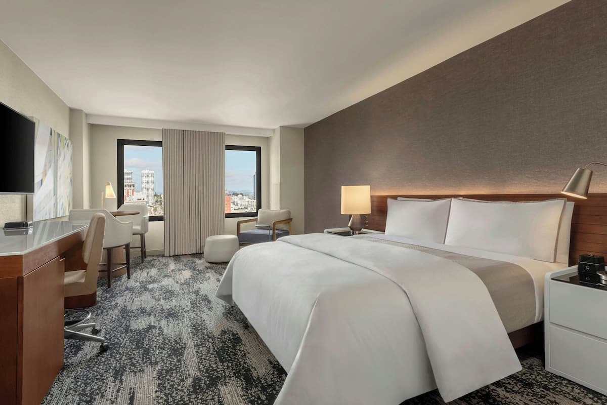 Habitación de hotel con una cama grande, un escritorio, una silla, televisión y vista a la ciudad.