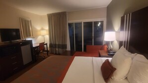 A hotel room with a large bed, a desk with a computer, a TV, and a view of the outside. - Ramada by Wyndham Sacramento (Sacramento)