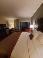 Una habitación de hotel con una cama grande, un escritorio con computadora, un televisor y vista al exterior.