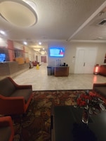 Un vestíbulo de hotel con mostrador de recepción, zona de estar y una pantalla de televisión.