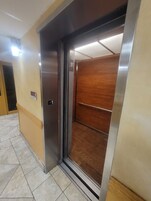 Un ascensor con interior metálico y un panel de madera en el lado derecho.