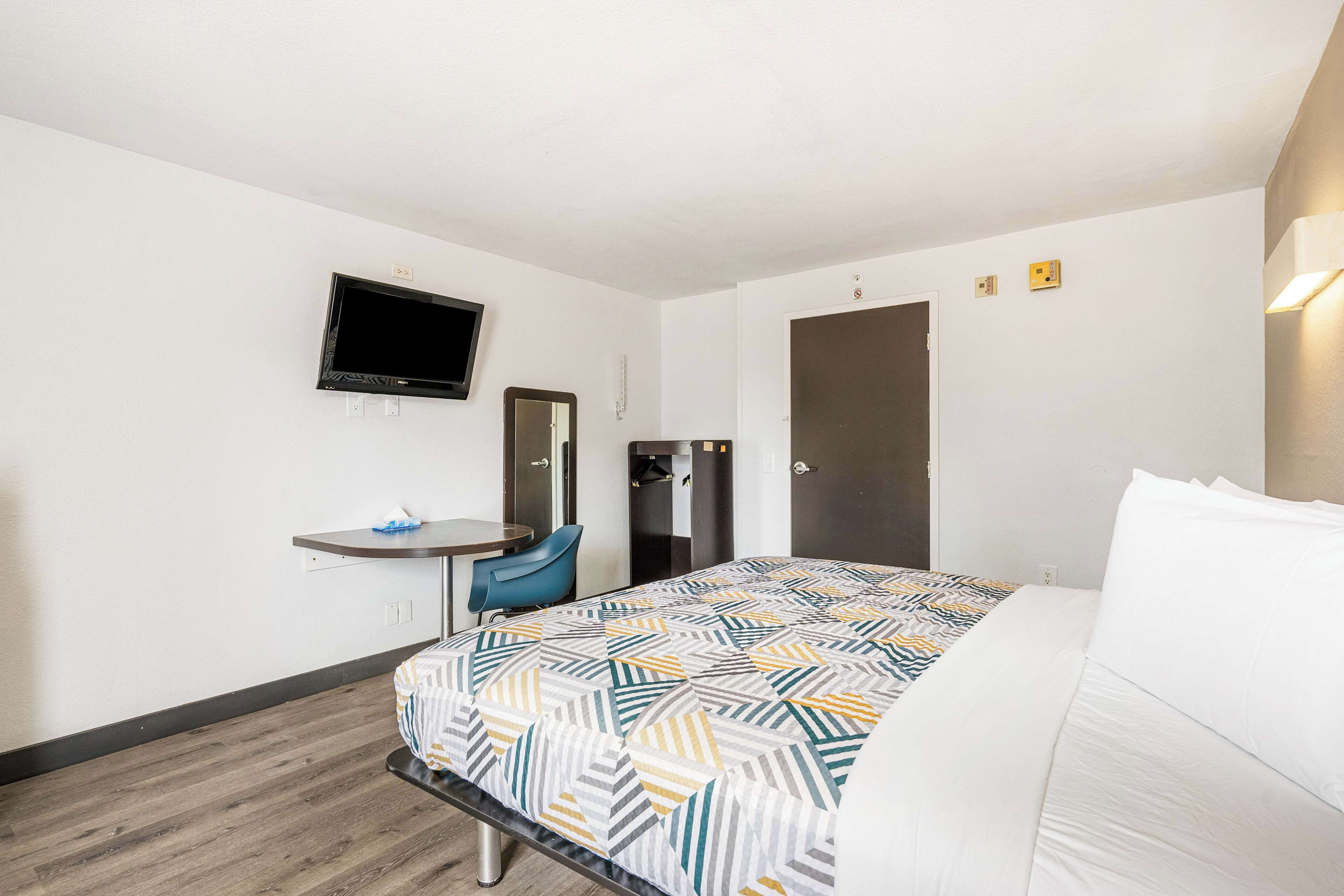 A hotel room with a bed, a desk, a chair, a television, and a wardrobe.