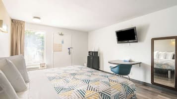 Habitación de hotel con cama, escritorio, silla, televisor y espejo.