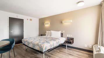 A hotel room with a bed, a desk, a chair, and a wall-mounted heater.