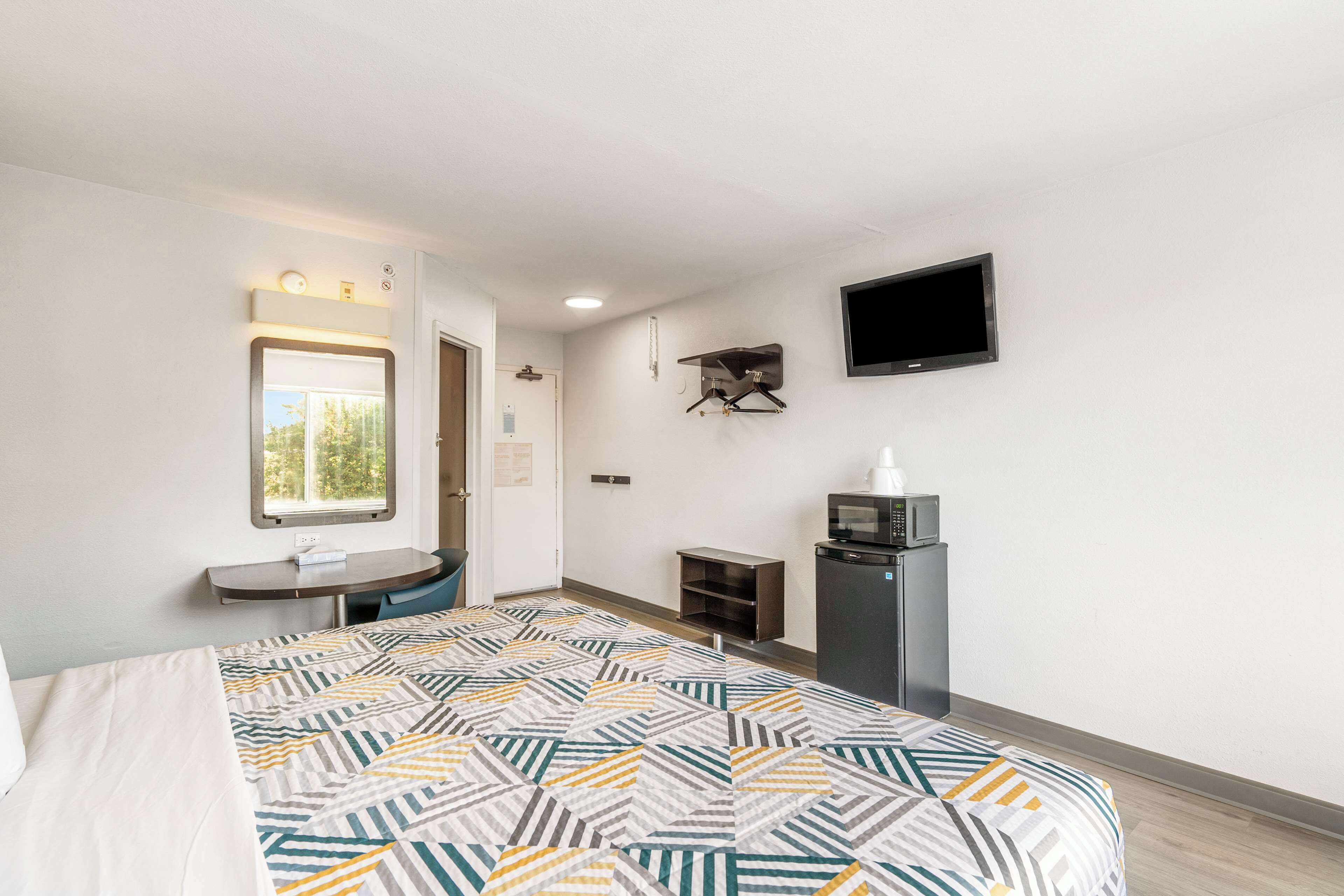 A hotel room with a bed, a desk, a TV, a microwave, and a window.