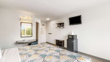 A hotel room with a bed, a desk, a TV, a microwave, and a window.