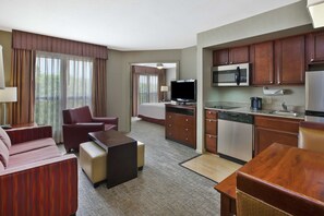A hotel room with a living area, a kitchenette, and a bedroom.