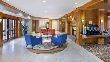 A hotel lobby with a reception desk, a red sofa, two blue armchairs, a coffee station, and a fireplace.