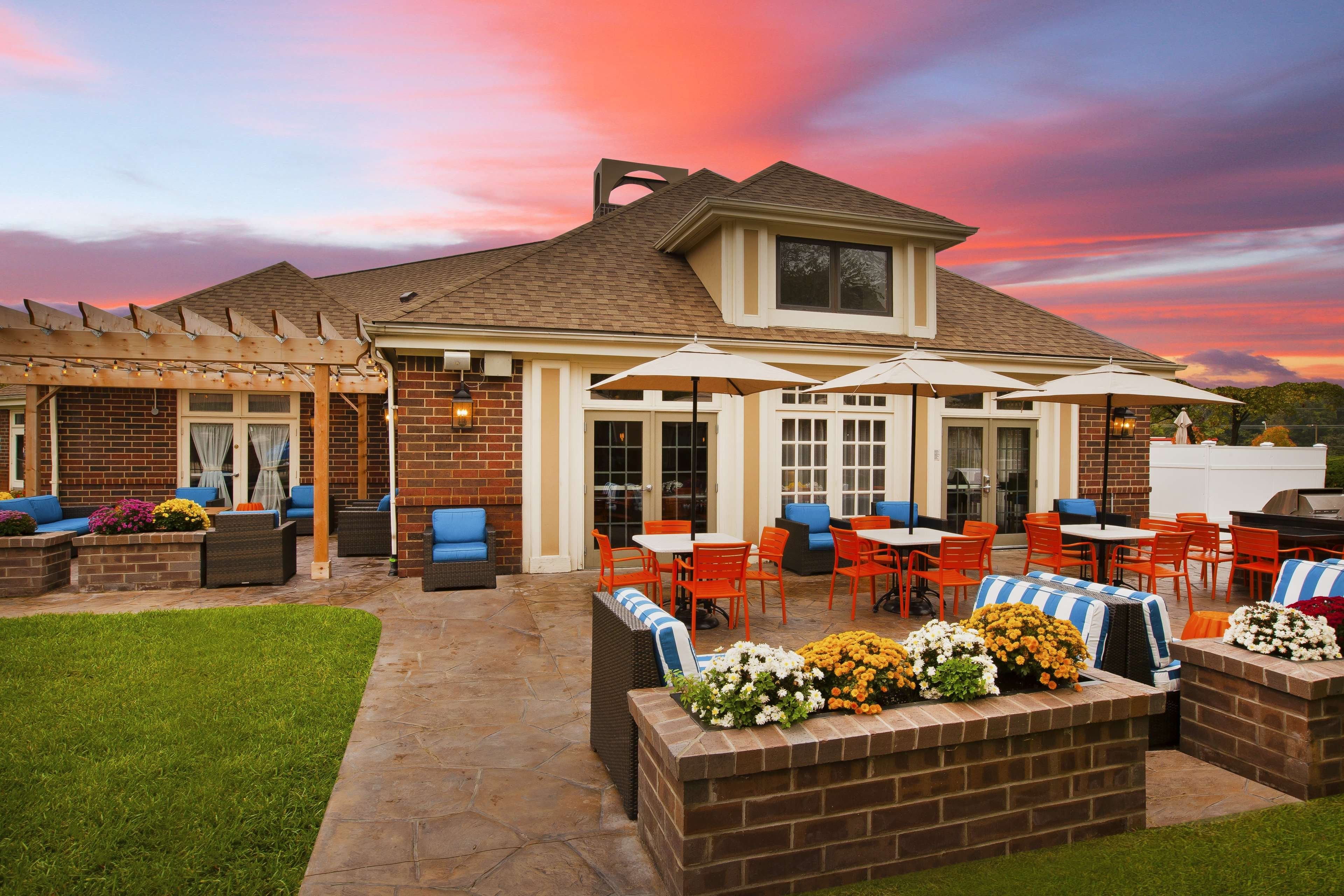 A patio area with outdoor seating, a barbecue grill, and a brick wall with flower planters.