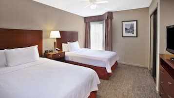 A hotel room with two beds, a nightstand with a lamp, a ceiling fan, a framed picture on the wall, and a television on a dresser.