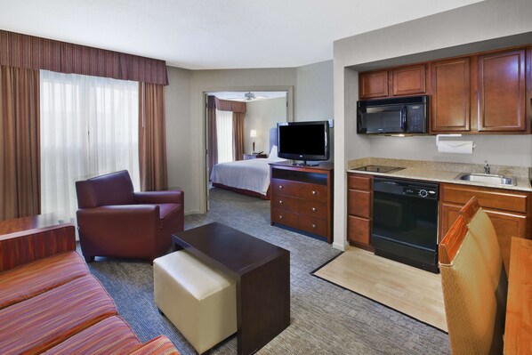 A hotel room with a sofa, a TV, a bed, a desk, and a kitchenette.