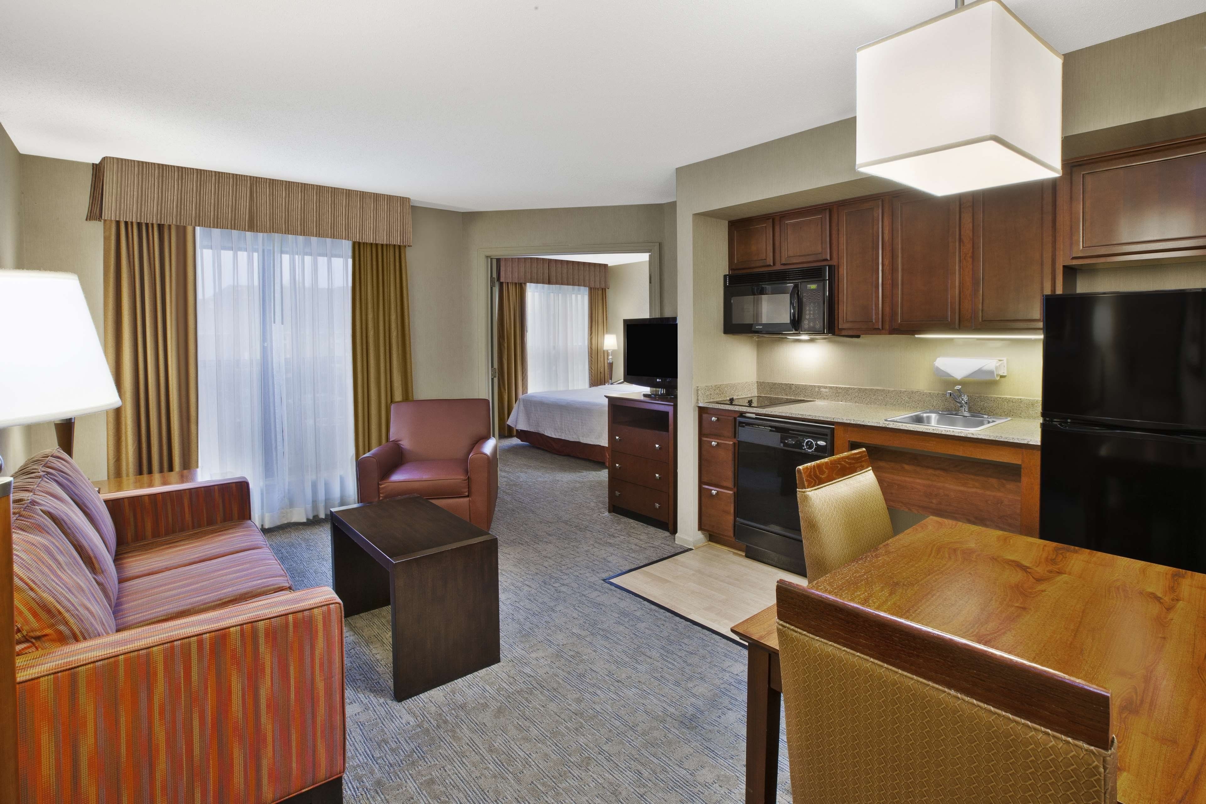 A hotel room with a sofa, armchair, dining table, kitchen area, and a bed.