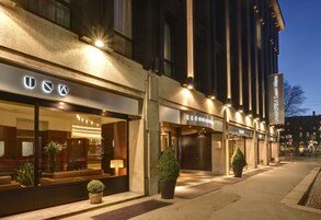 Η πρόσοψη ενός ξενοδοχείου με φωτεινές επιγραφές, μεγάλα παράθυρα και φυτά σε γλάστρες.
