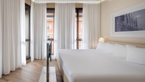 Ein Hotelzimmer mit einem großen Bett, weißen Vorhängen, einem gerahmten Bild an der Wand und Blick auf Gebäude.