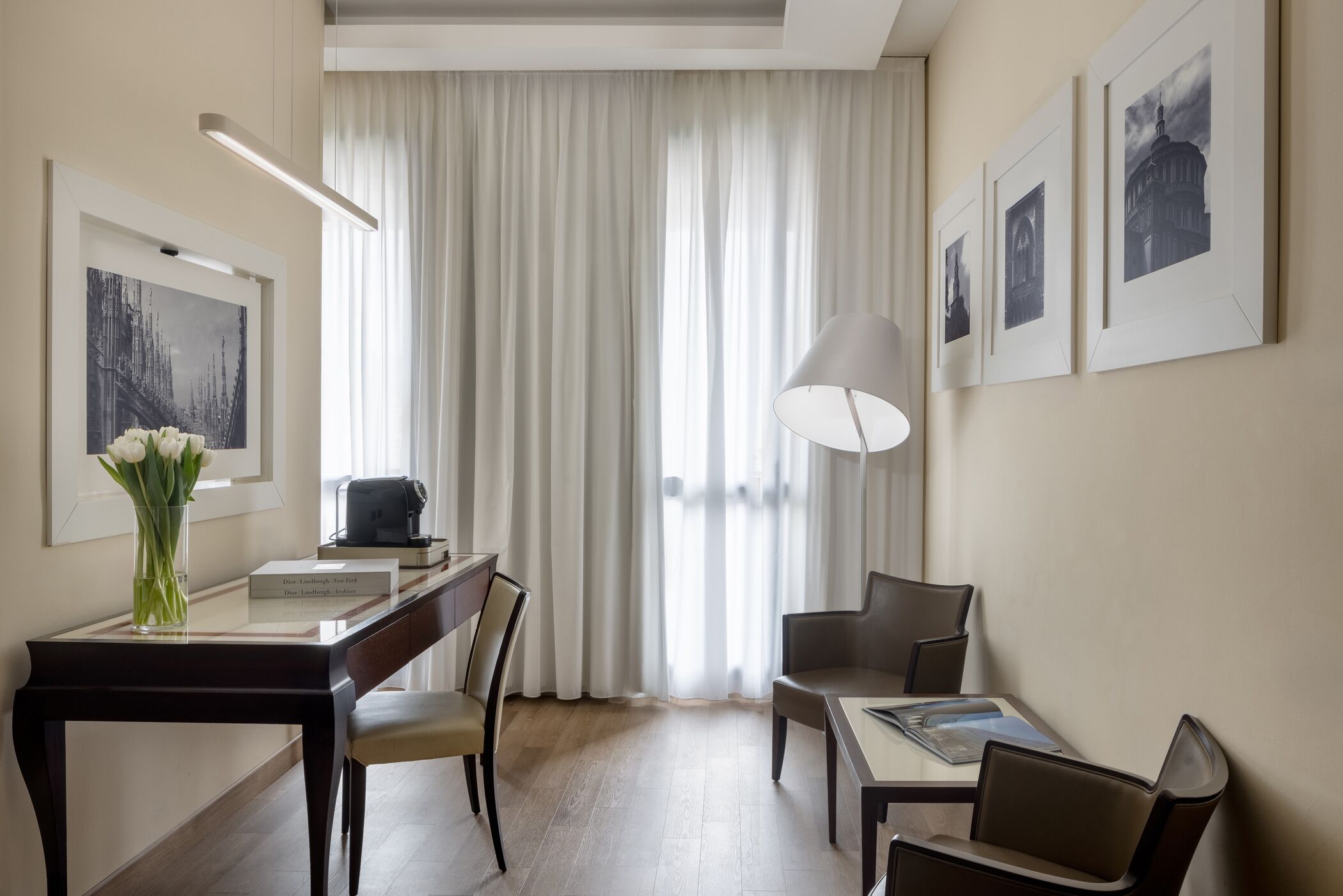 A hotel room with a dining area, a desk, a lamp, and a large window with curtains.