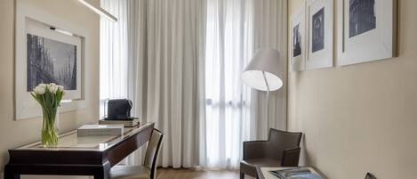 A hotel room with a dining area, a desk, a lamp, and a large window with curtains.
