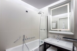 Un baño moderno con ducha de vidrio, una bañera blanca y un espejo grande sobre un lavamanos.