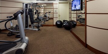A gym with cardio machines, weight machines, and exercise balls, featuring a carpeted floor and mirrored walls.