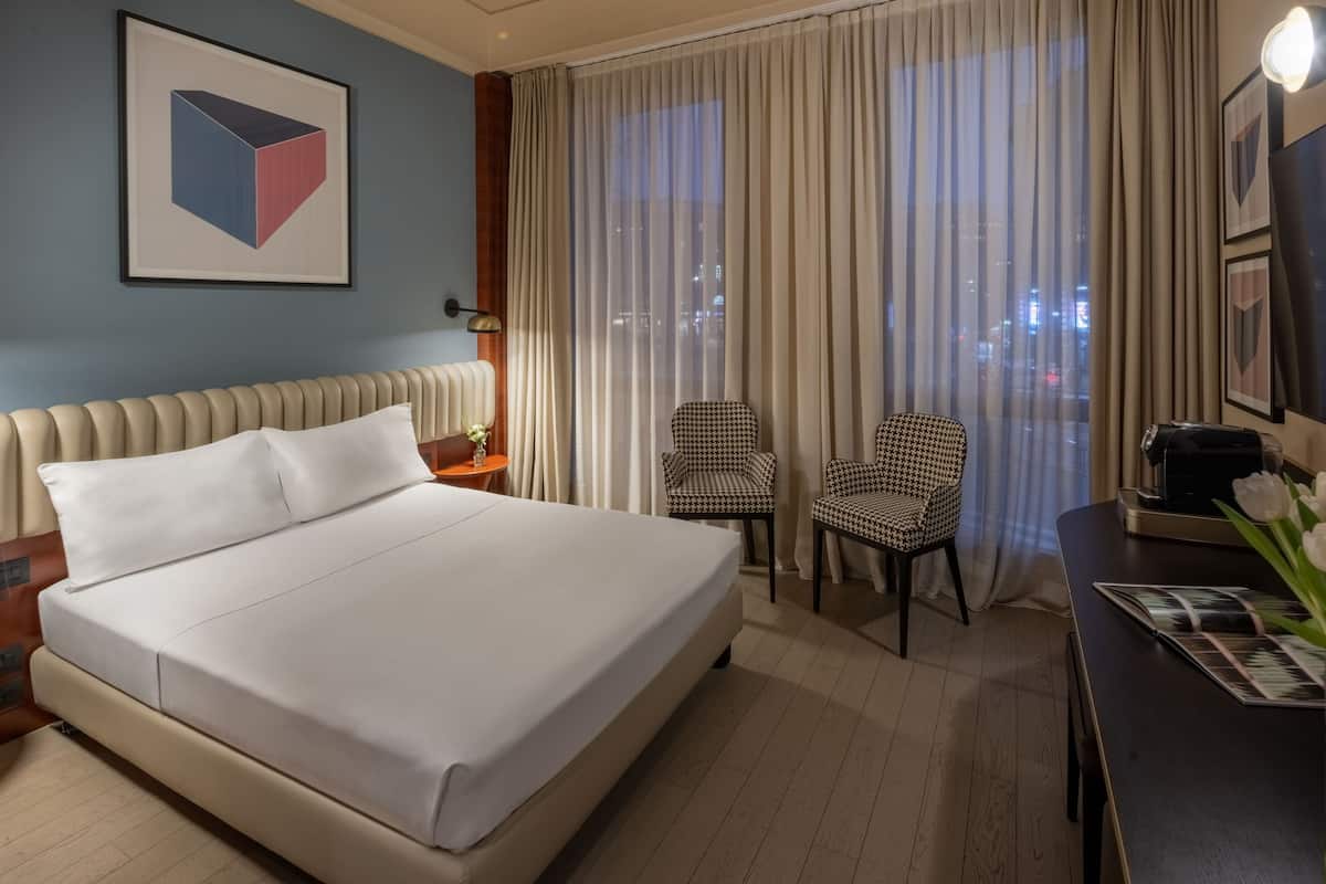 A hotel room with a large bed, two chairs, a desk, and a window with curtains.