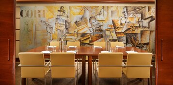 Une salle de conférence avec une table en bois, des chaises de couleur beige et un grand tableau abstrait accroché au mur.