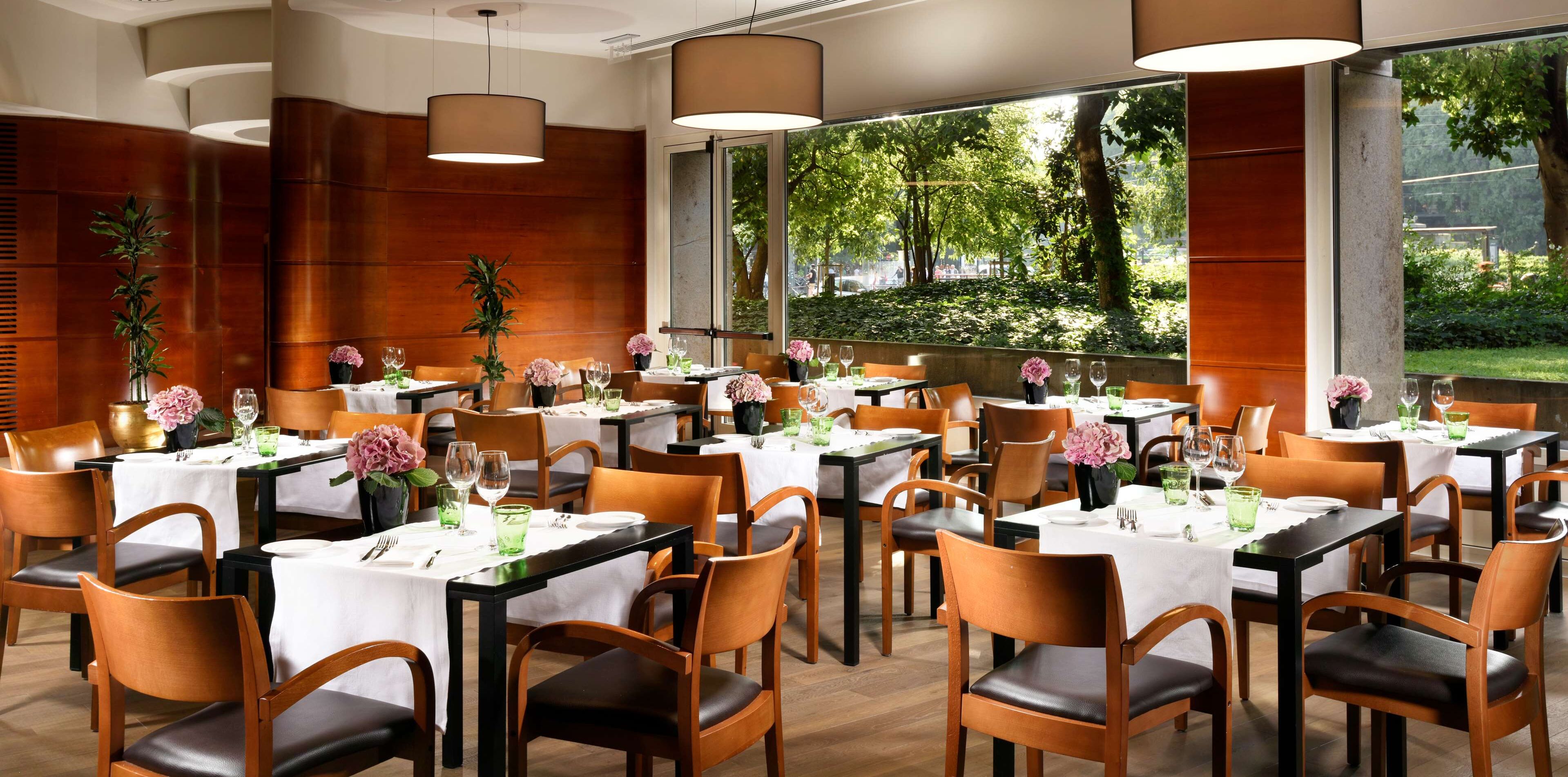 Ein Restaurant mit mehreren Tischen, jeder Tisch mit weißer Tischdecke, Stühlen und floraler Dekoration.