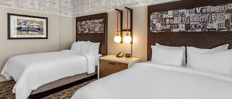 Habitación de hotel con dos camas, una mesita de noche, un teléfono y una pared con texto impreso.