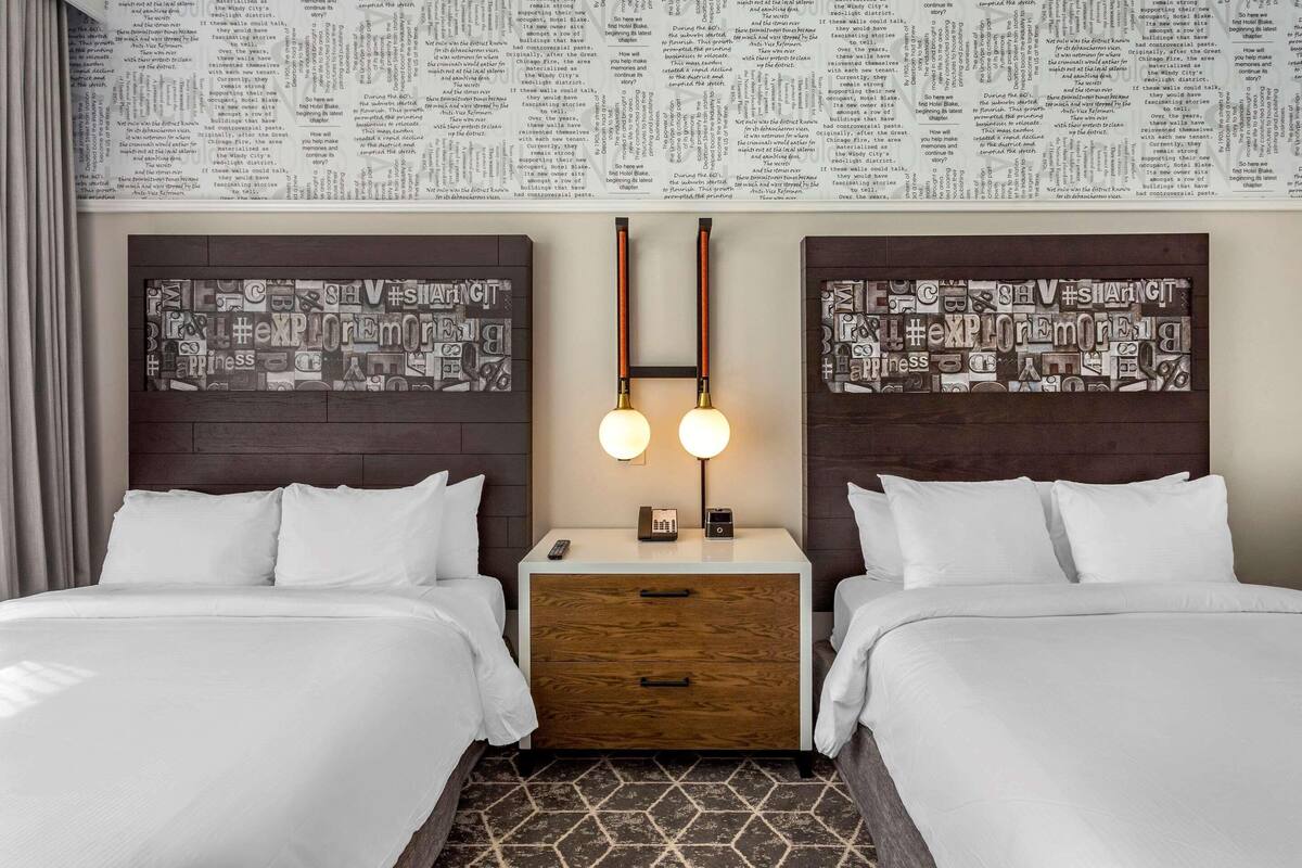 A hotel room with two beds, a wooden nightstand, a wall clock, and a patterned wallpaper.