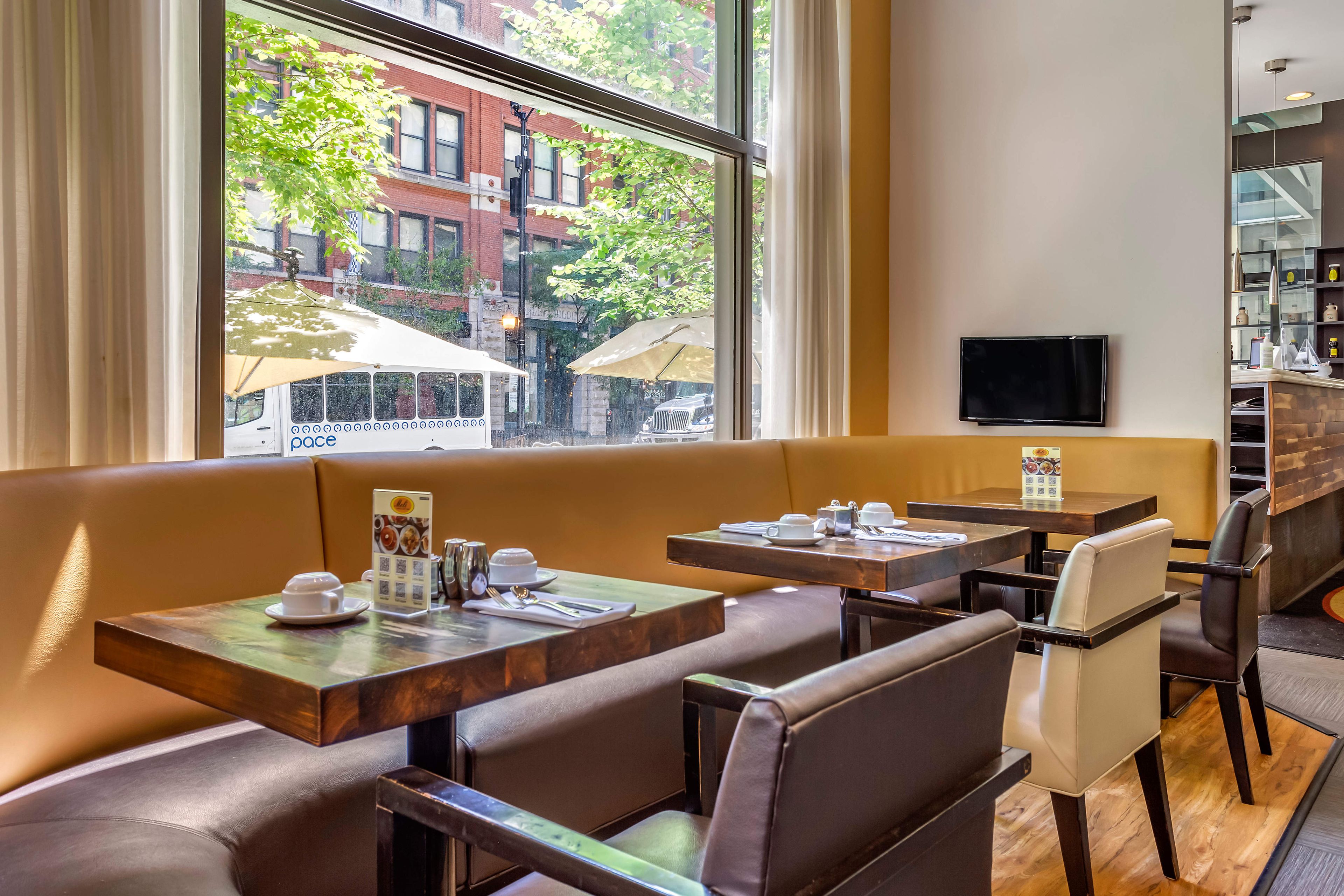 A restaurant with booths and tables, a television on the wall, and a view of the street outside.