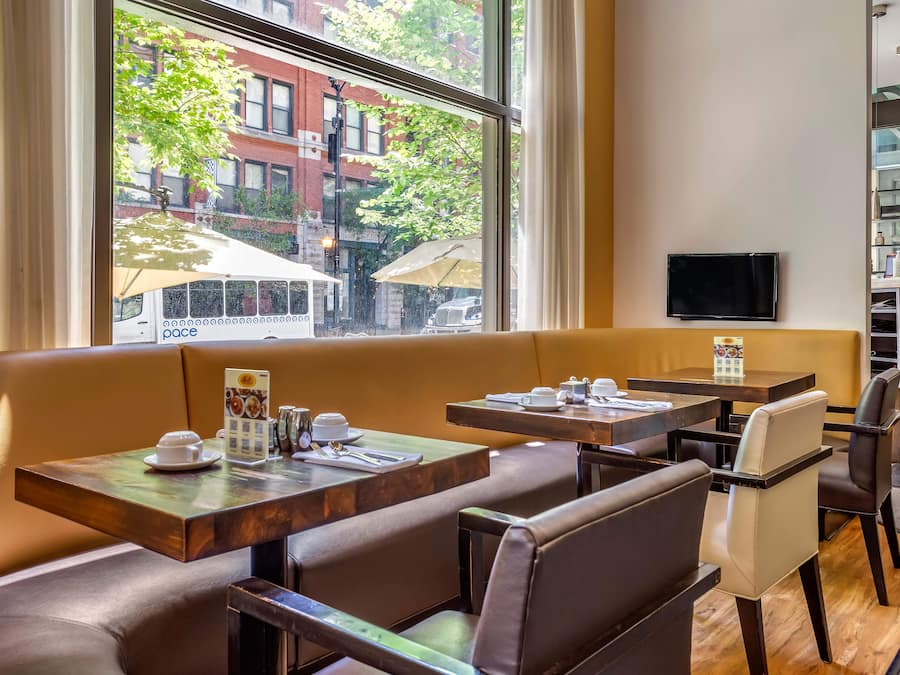 Um restaurante com cabines e mesas, uma televisão na parede e vista para a rua.