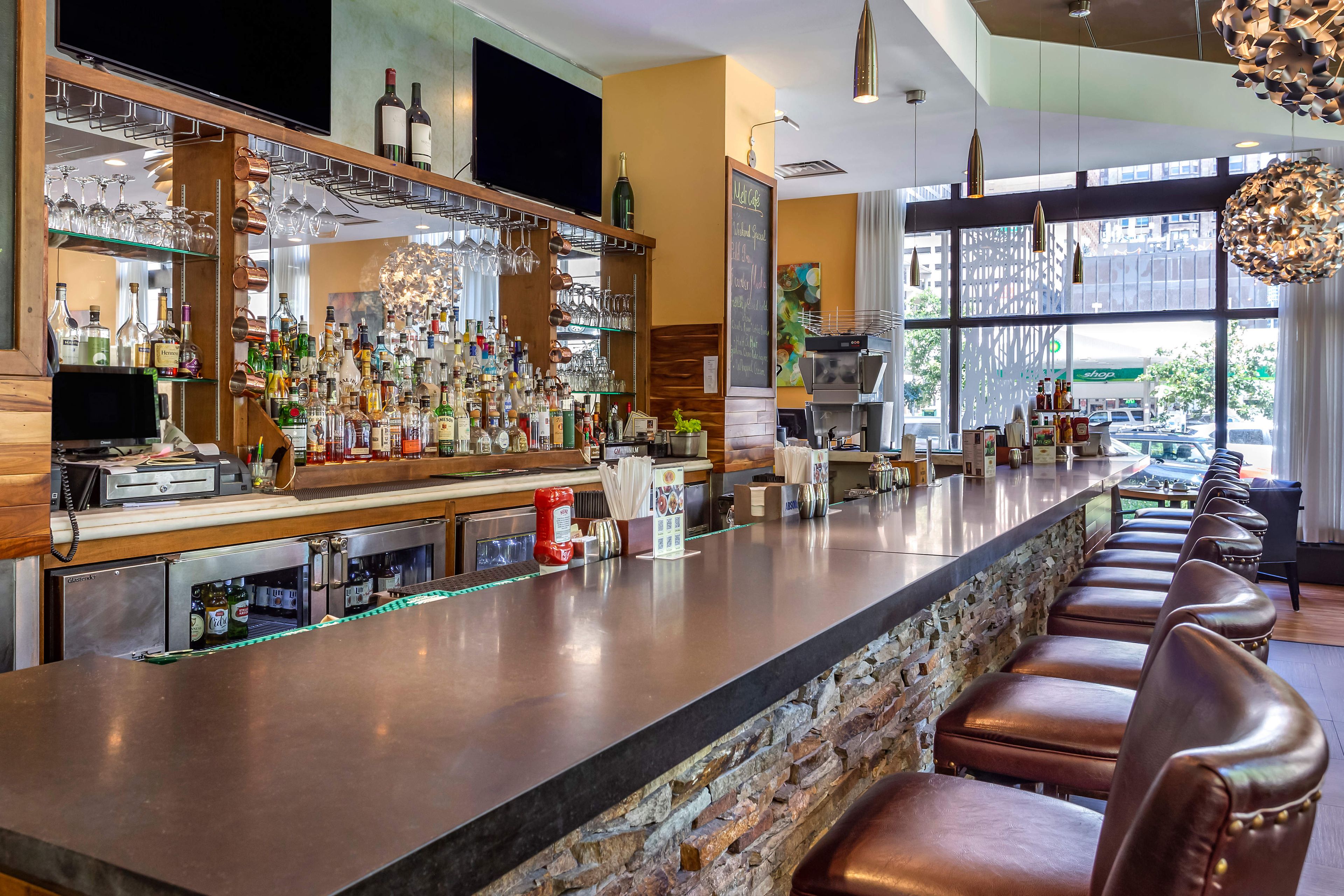 A bar area with a long counter, multiple liquor bottles, and a variety of glasses.